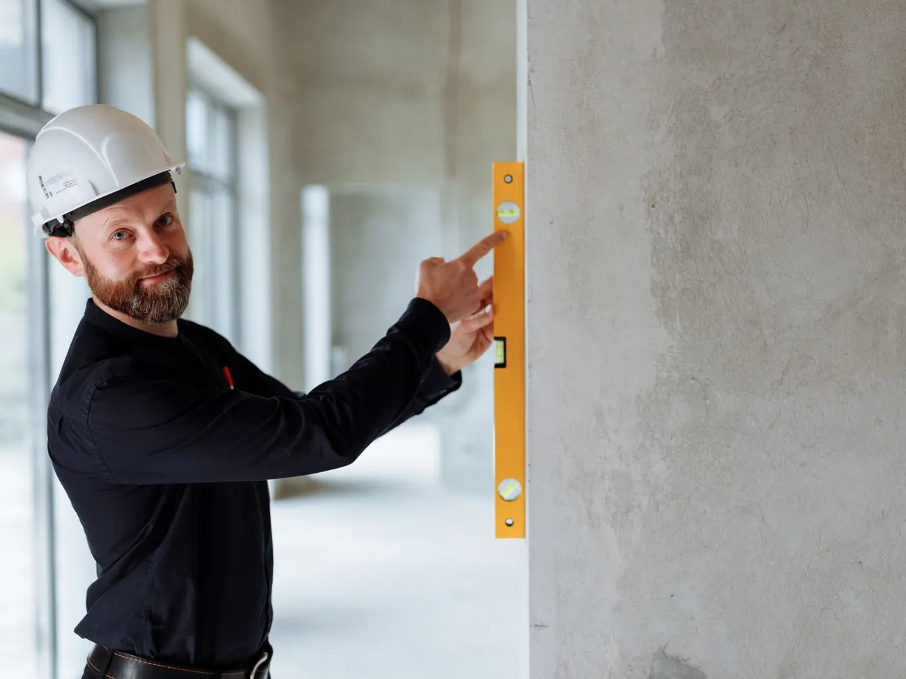 Engenheiro com capacete de segurança conferindo o prumo de uma parede de concreto com nível de bolha.