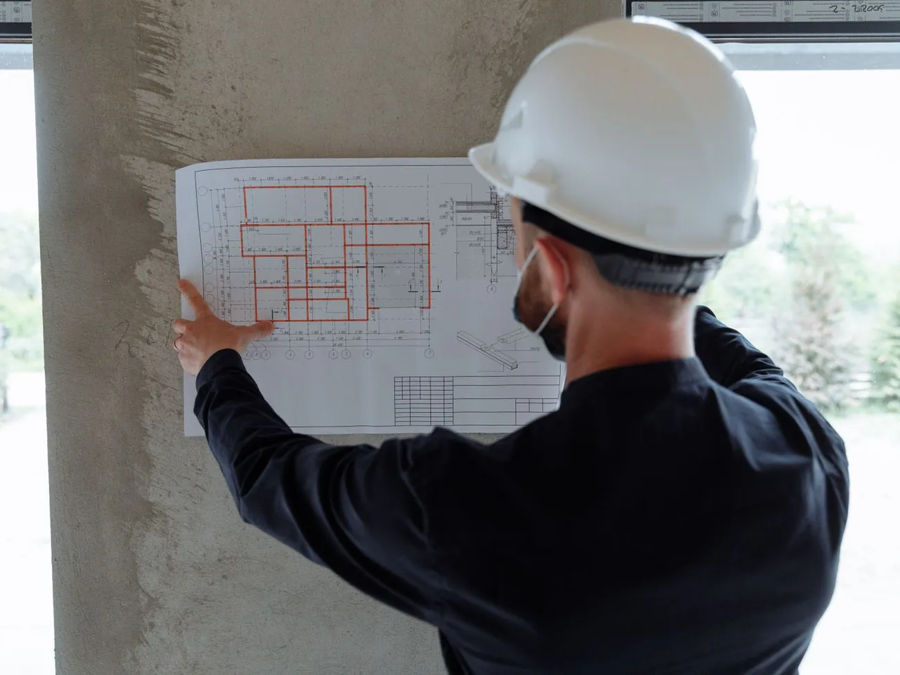 Engenheiro de capacete analisando uma prancha de projeto em obra.